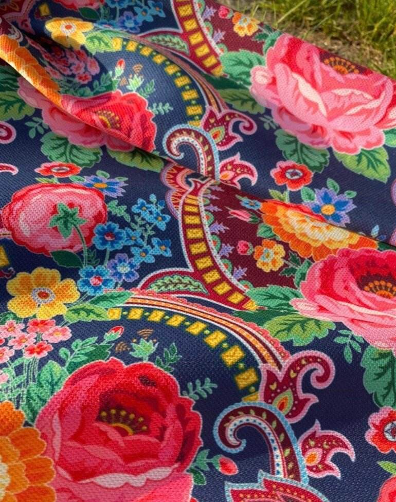 Close-up of vibrant ethnic patterned fabric with colorful floral and geometric designs on dark background, suitable for upholstery and outdoor use.