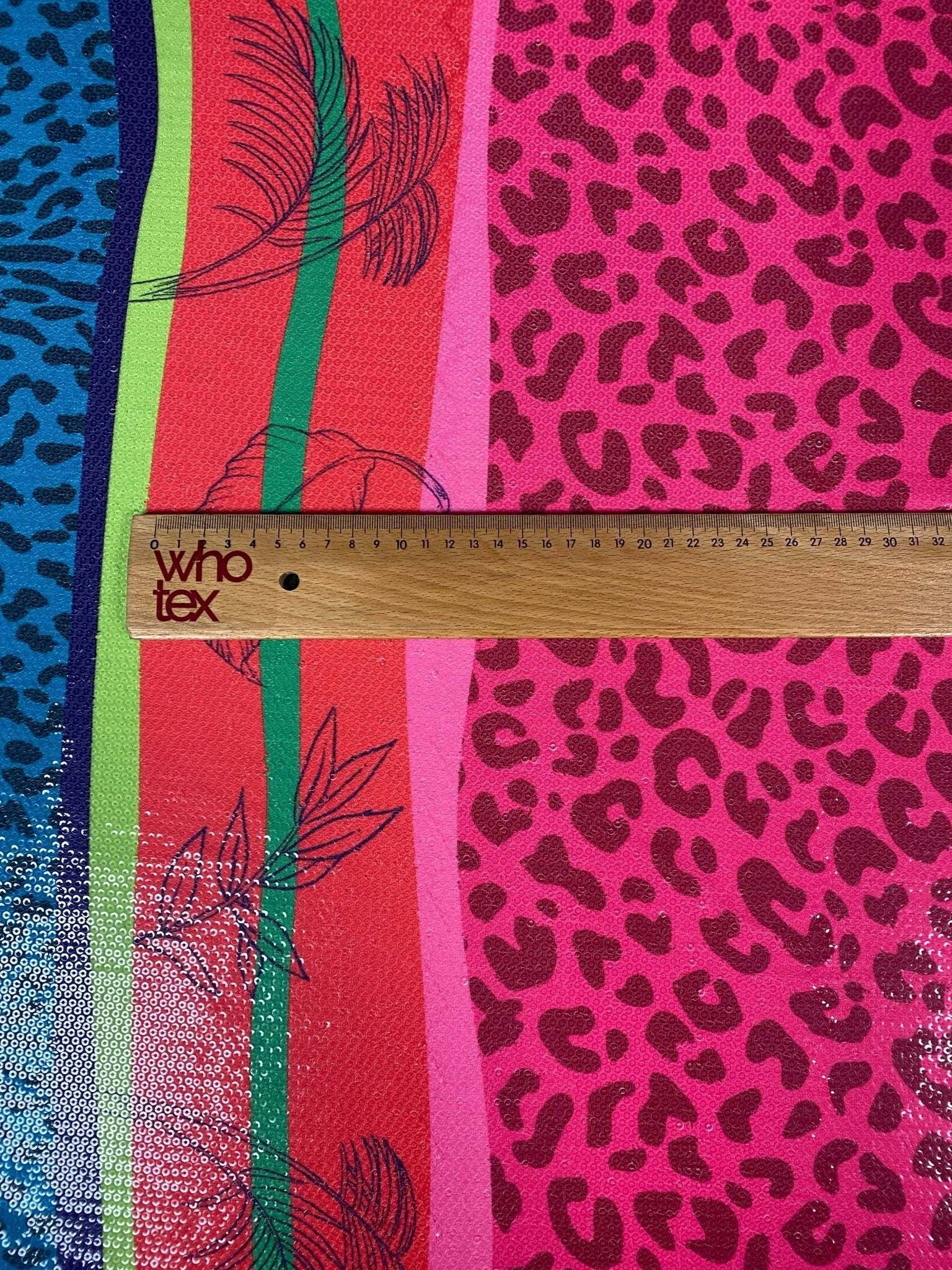 Close-up of vibrant exotic animal print sequin fabric with 2-way stretch and colorful patterns alongside a wooden ruler