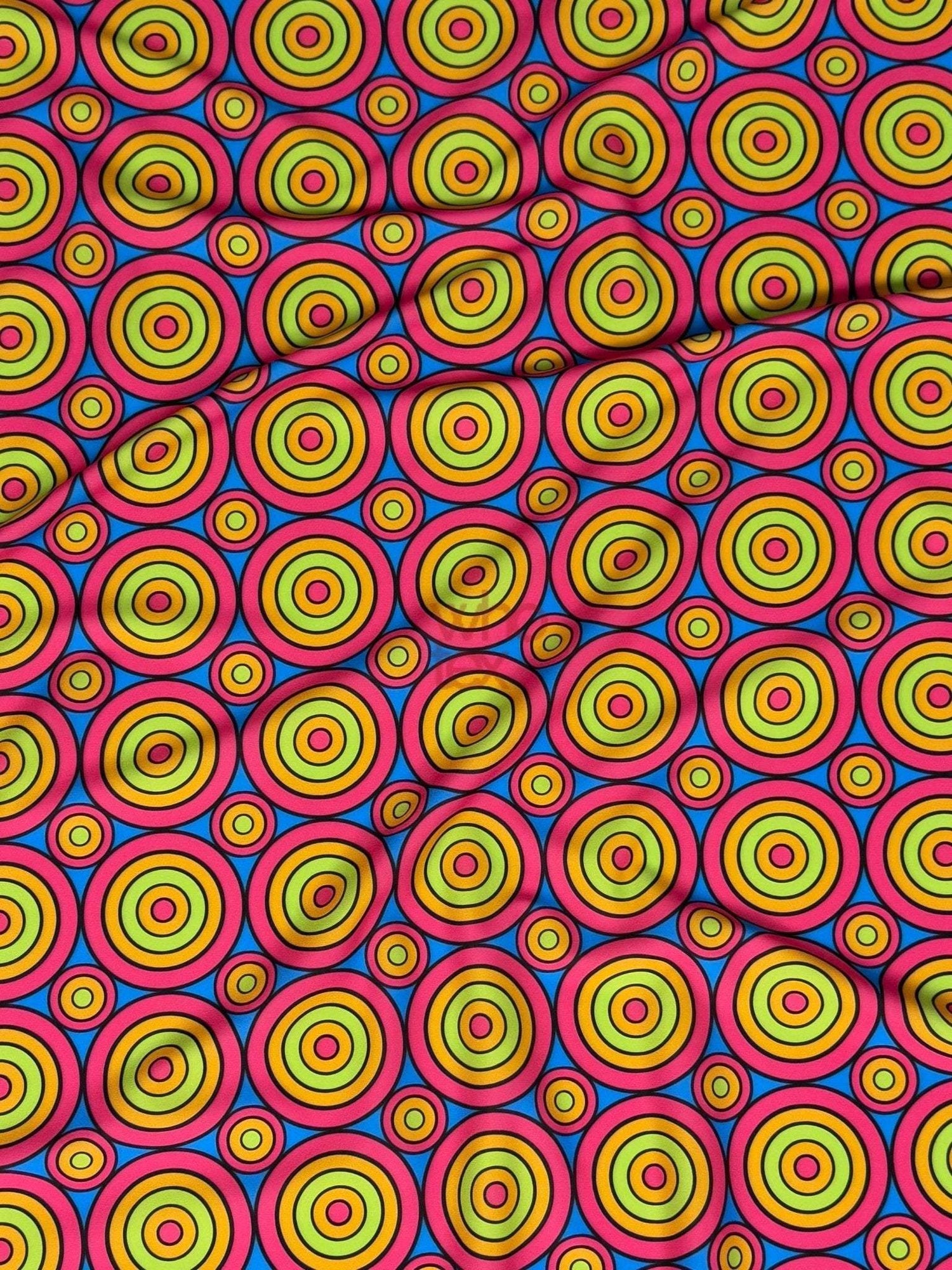 Bright colorful geometric circles print fabric with vibrant concentric ring patterns in yellow, green, blue, and red on a pink background.