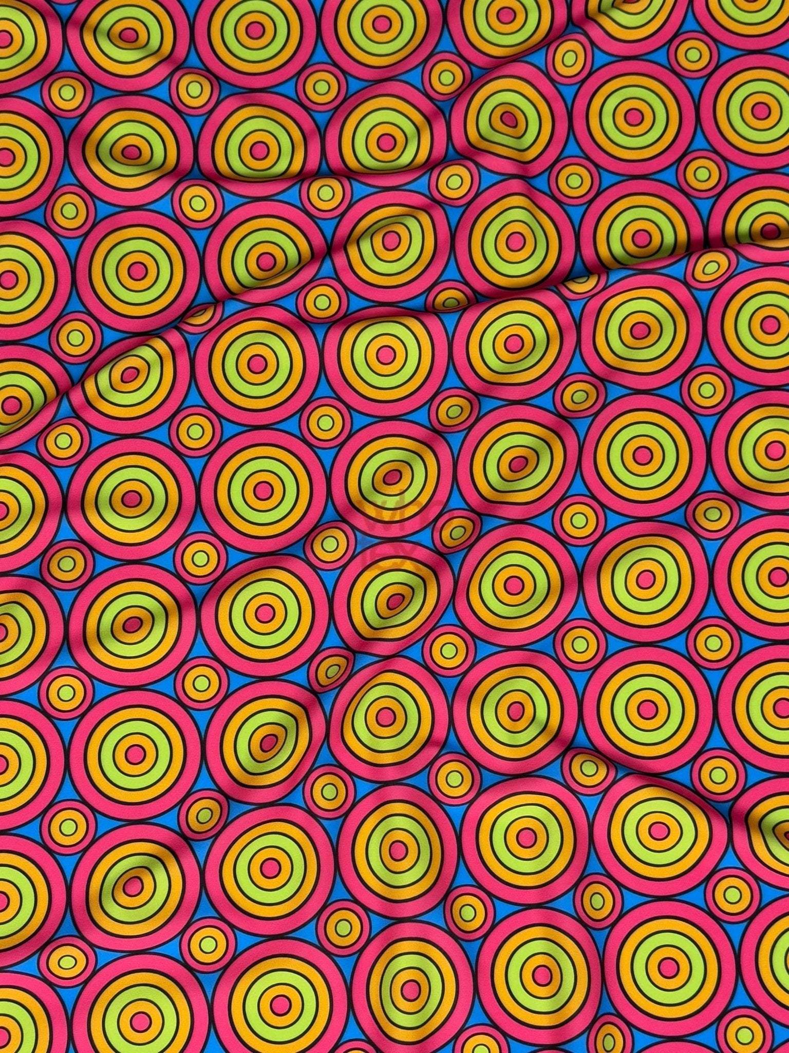Bright colorful geometric circles print fabric with vibrant concentric ring patterns in yellow, green, blue, and red on a pink background.