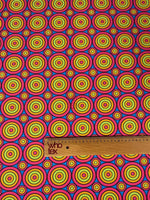 Colorful geometric circles print fabric with vibrant concentric circles in red, yellow, green, and blue, shown with a wooden ruler for scale
