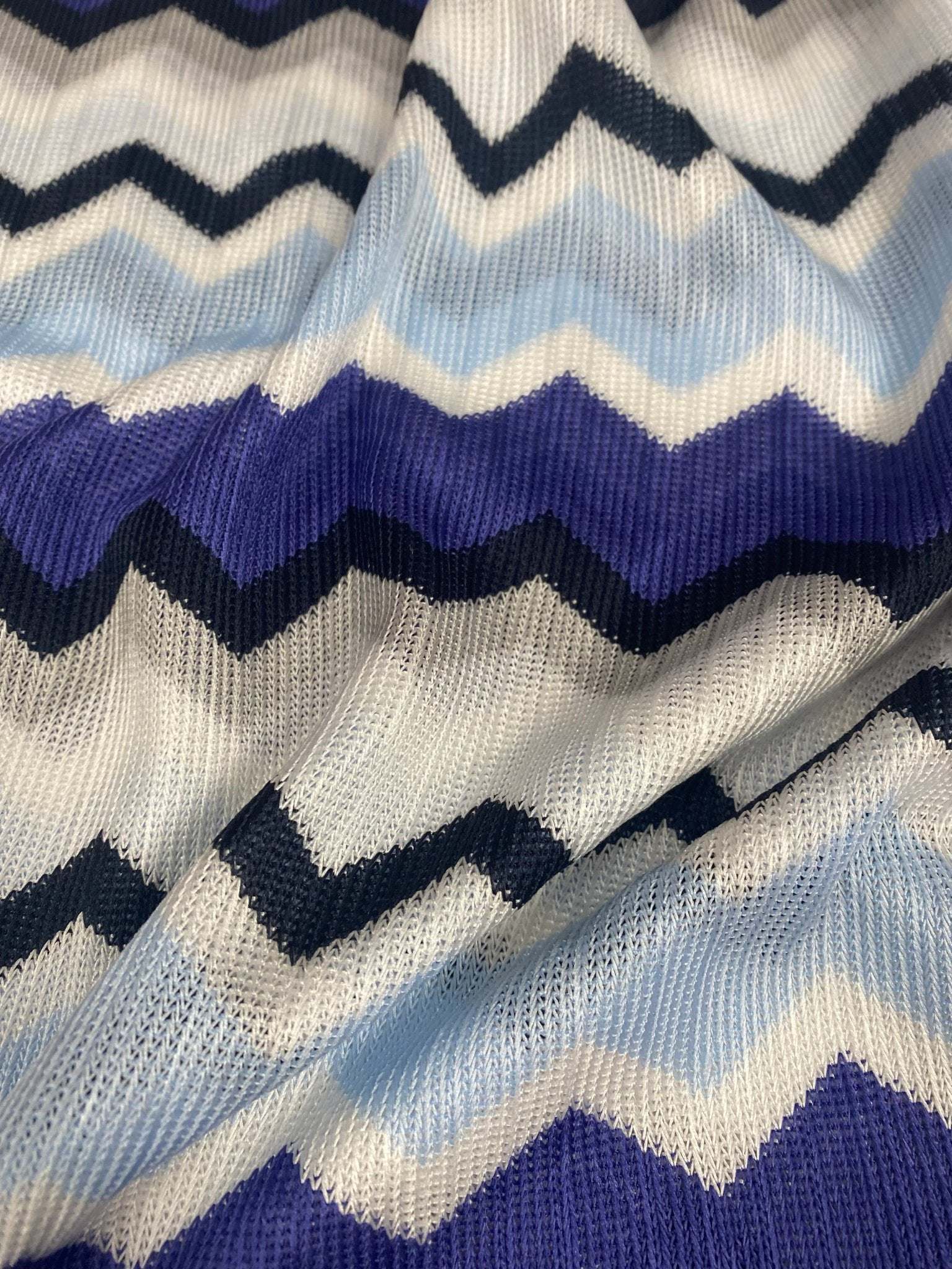 Close-up of blue, purple, beige geometric zigzag patterned woven fabric with textured knit mesh design