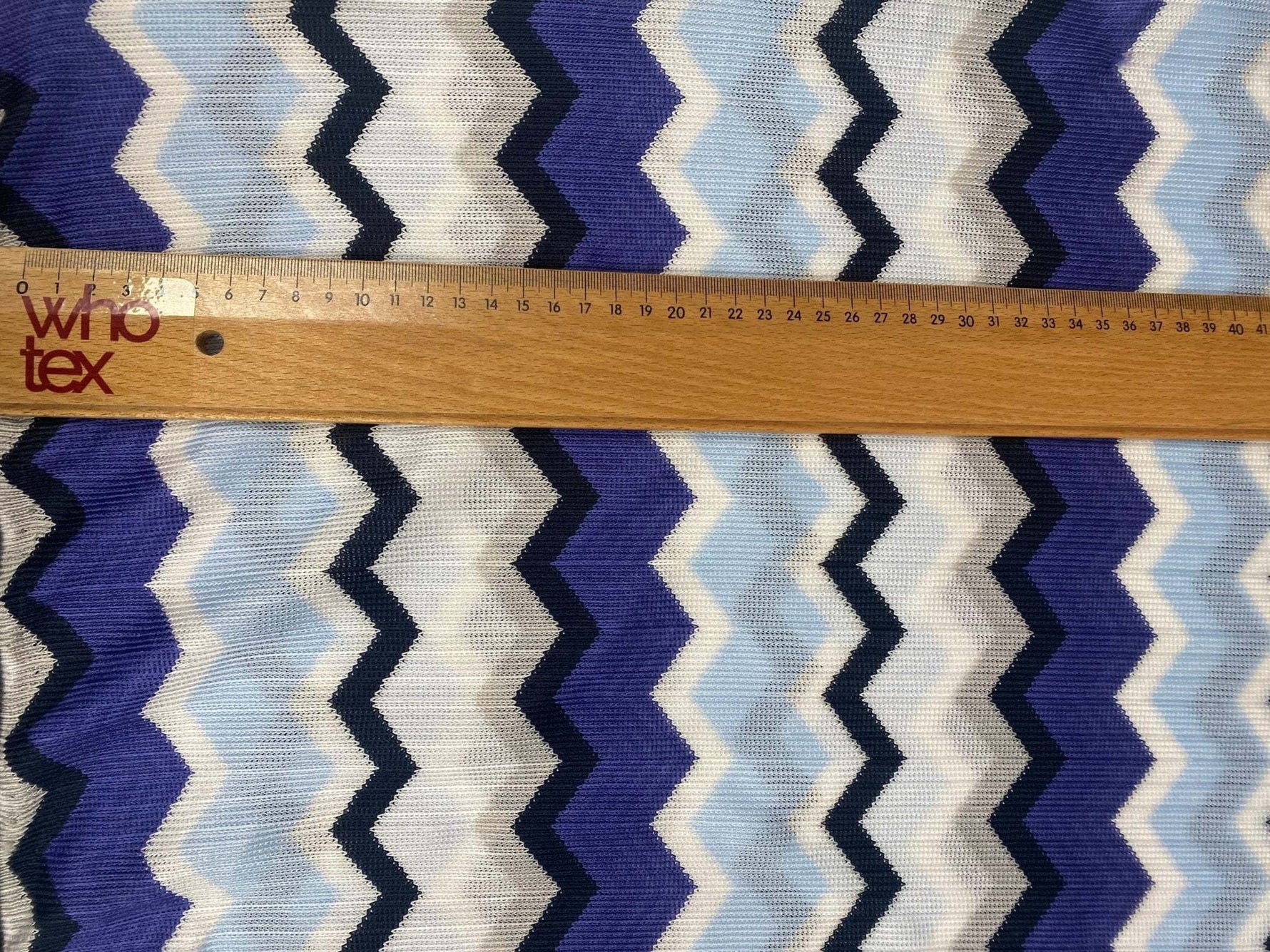 Blue, purple, and beige geometric zigzag patterned woven fabric with ruler for scale