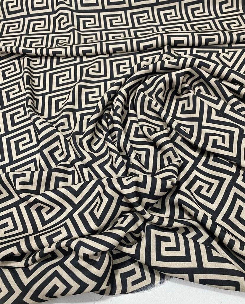 Black and beige Greek key patterned fabric with 150cm width, shown draped and folded.