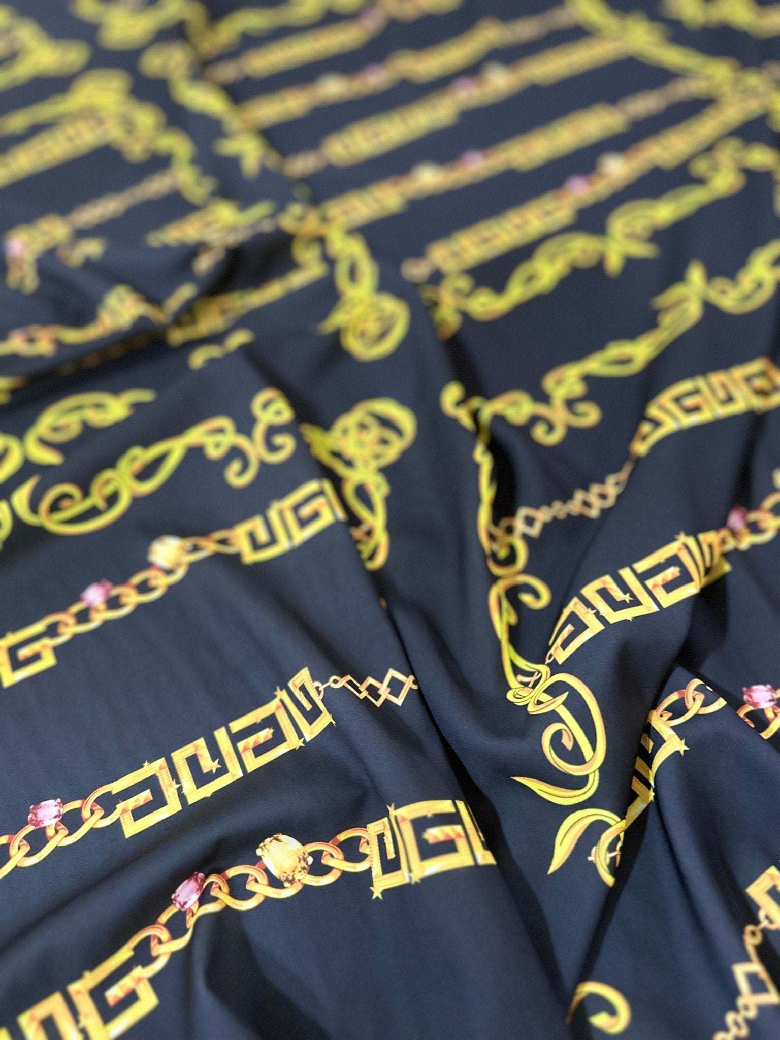 Close-up of black fabric with gold Greek key and chain pattern, luxurious upholstery and fashion textile
