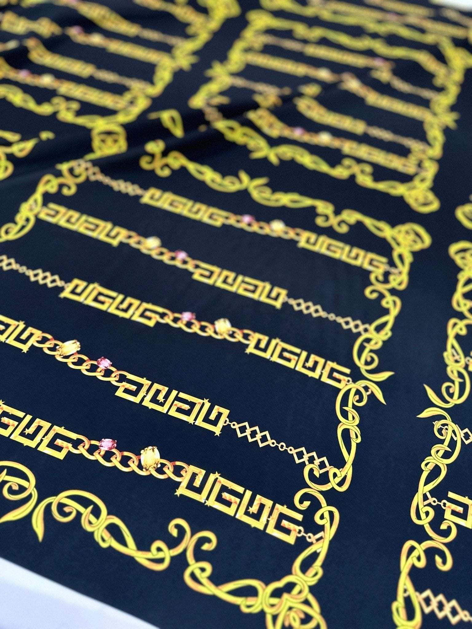 Close-up of Gold Greek Key Fabric with intricate chain and scroll patterns on a dark background
