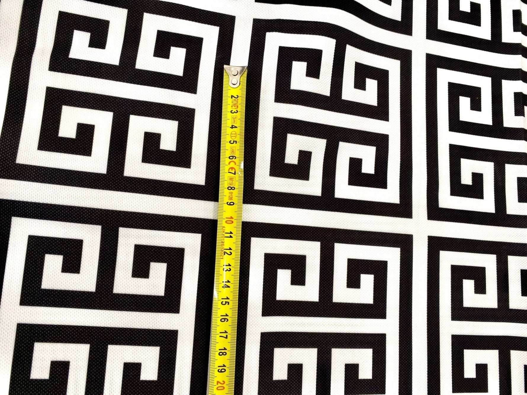 Close-up of black and white Greek key print upholstery fabric with measuring tape showing scale