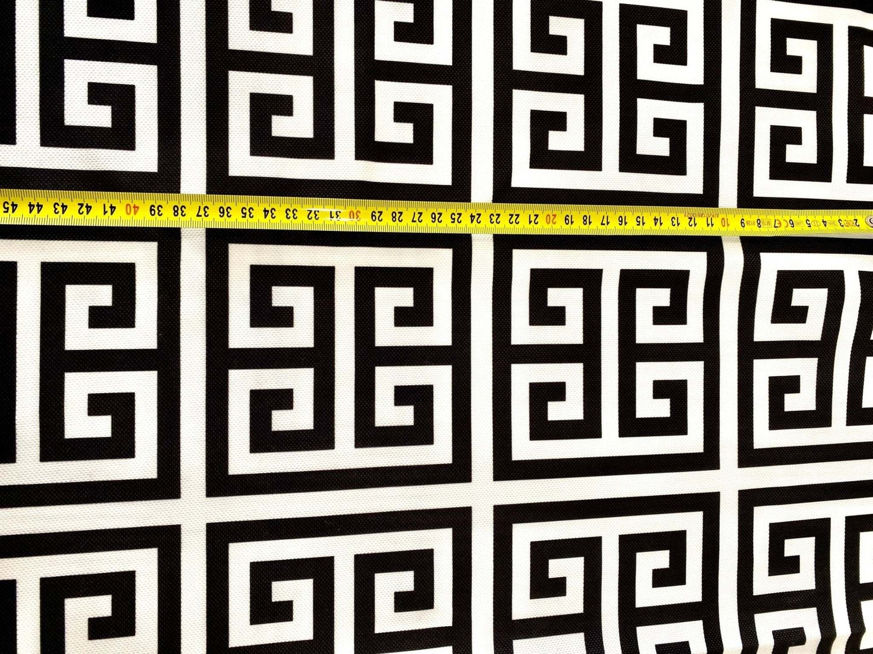 Greek Key Print Upholstery Fabric with black and white geometric pattern and measuring tape showing scale
