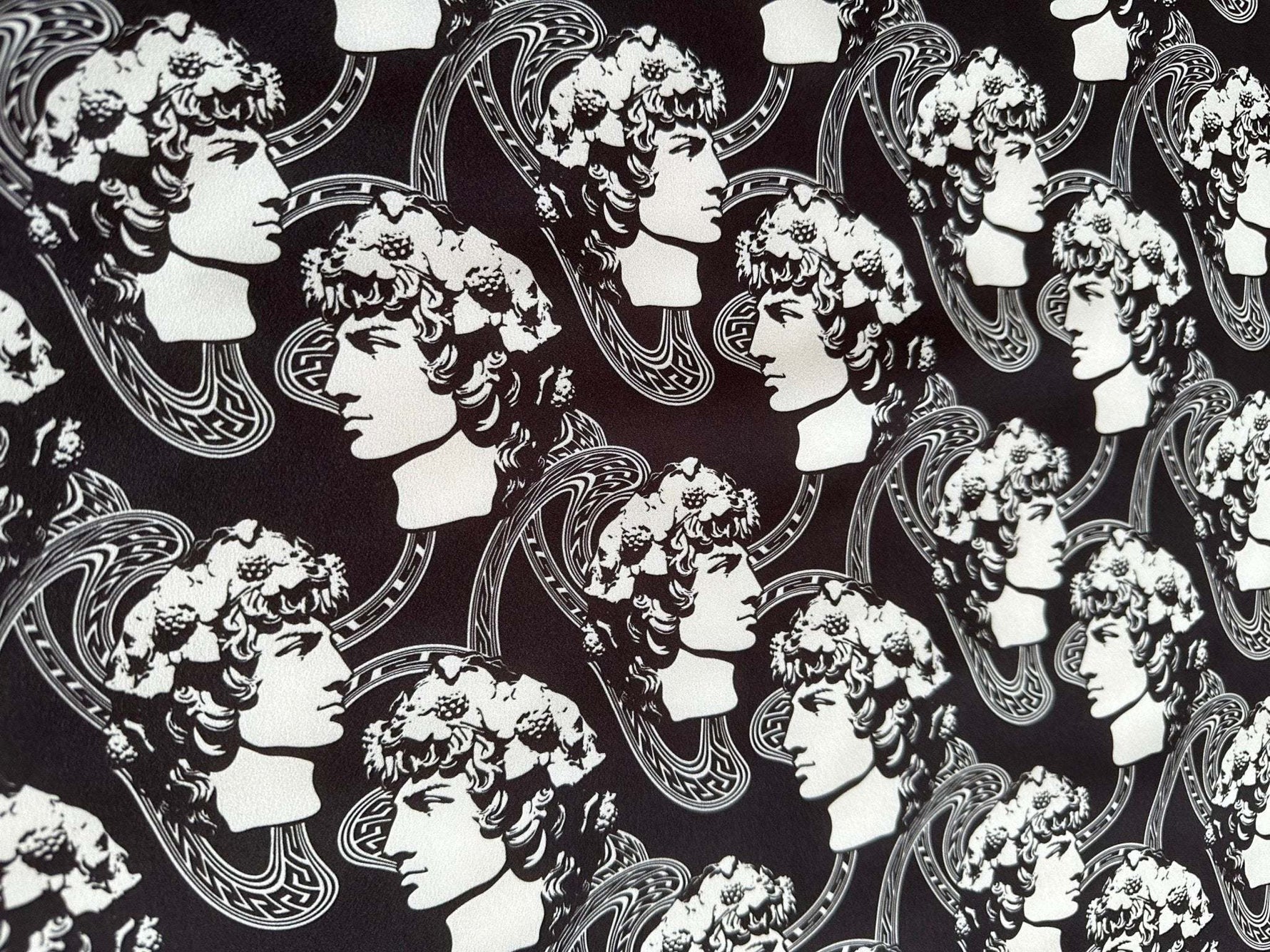 Black and white Greek crepe fabric featuring repeated classical Roman profile designs and intricate patterns