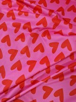 Pink cotton fabric with red heart prints, soft and suitable for sewing and crafting projects