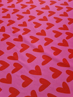 Pink cotton fabric with red heart print pattern for sewing and crafting projects