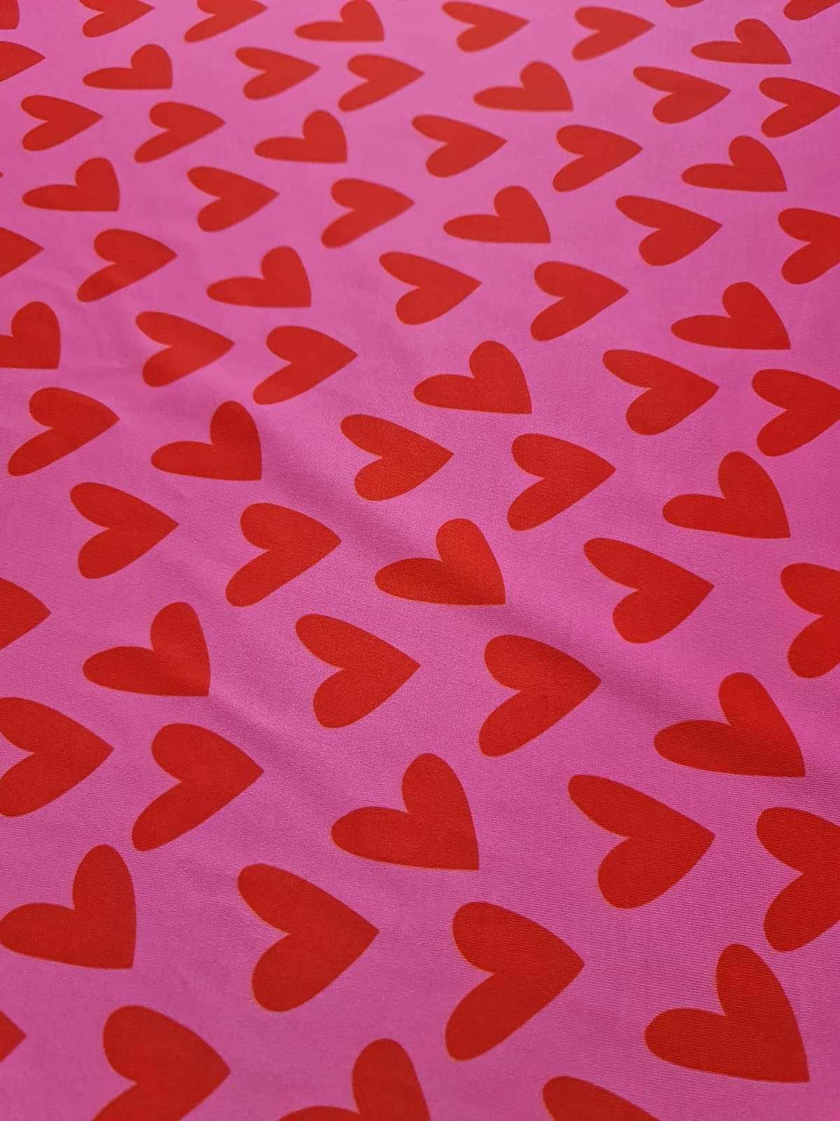 Pink cotton fabric with red heart print pattern for sewing and crafting projects