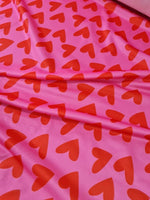 Pink cotton fabric with red heart prints for crafting and sewing projects