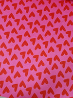 Pink cotton fabric with red heart print pattern for crafting and sewing projects