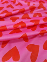Pink cotton fabric with red heart print pattern, ideal for crafting and sewing projects