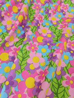 Colorful floral fabric with vibrant pink, blue, yellow flowers and green leaves pattern