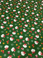 Green Santa Claus Christmas fabric with festive Santa faces, stockings, candy canes, and snowflakes on a green background