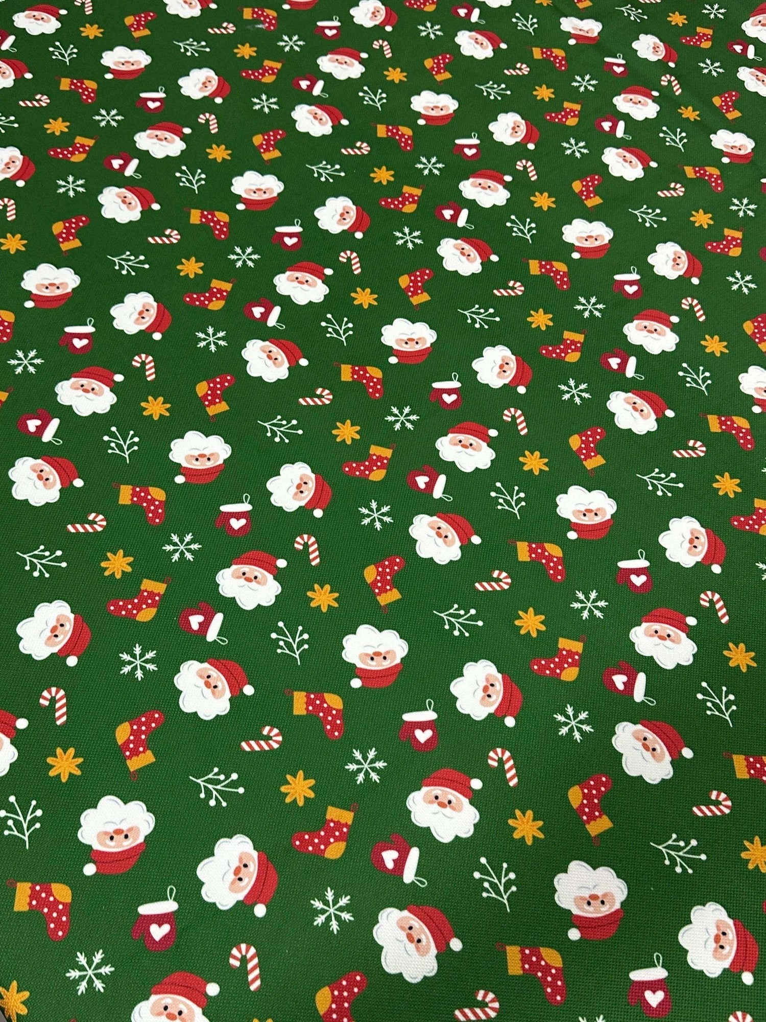 Green Santa Claus Christmas fabric with festive Santa faces, stockings, candy canes, and snowflakes on a green background
