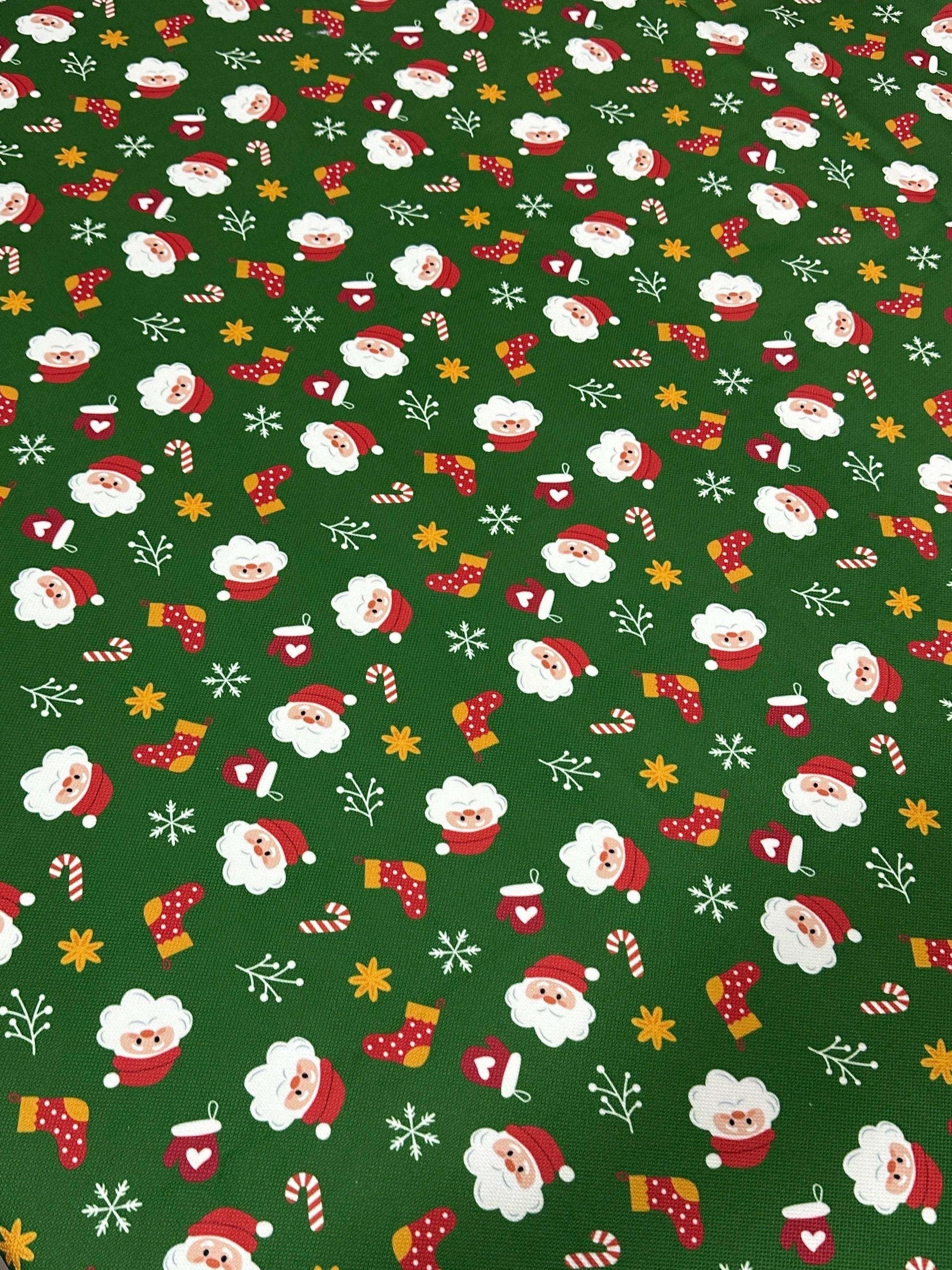 Green Santa Claus Christmas fabric with festive Santa faces, stockings, candy canes, and snowflakes on a green background