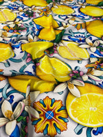 Close-up of lemon blue Spanish pattern fabric featuring vibrant yellow lemons, blue and orange floral motifs, and green leaves on a white background