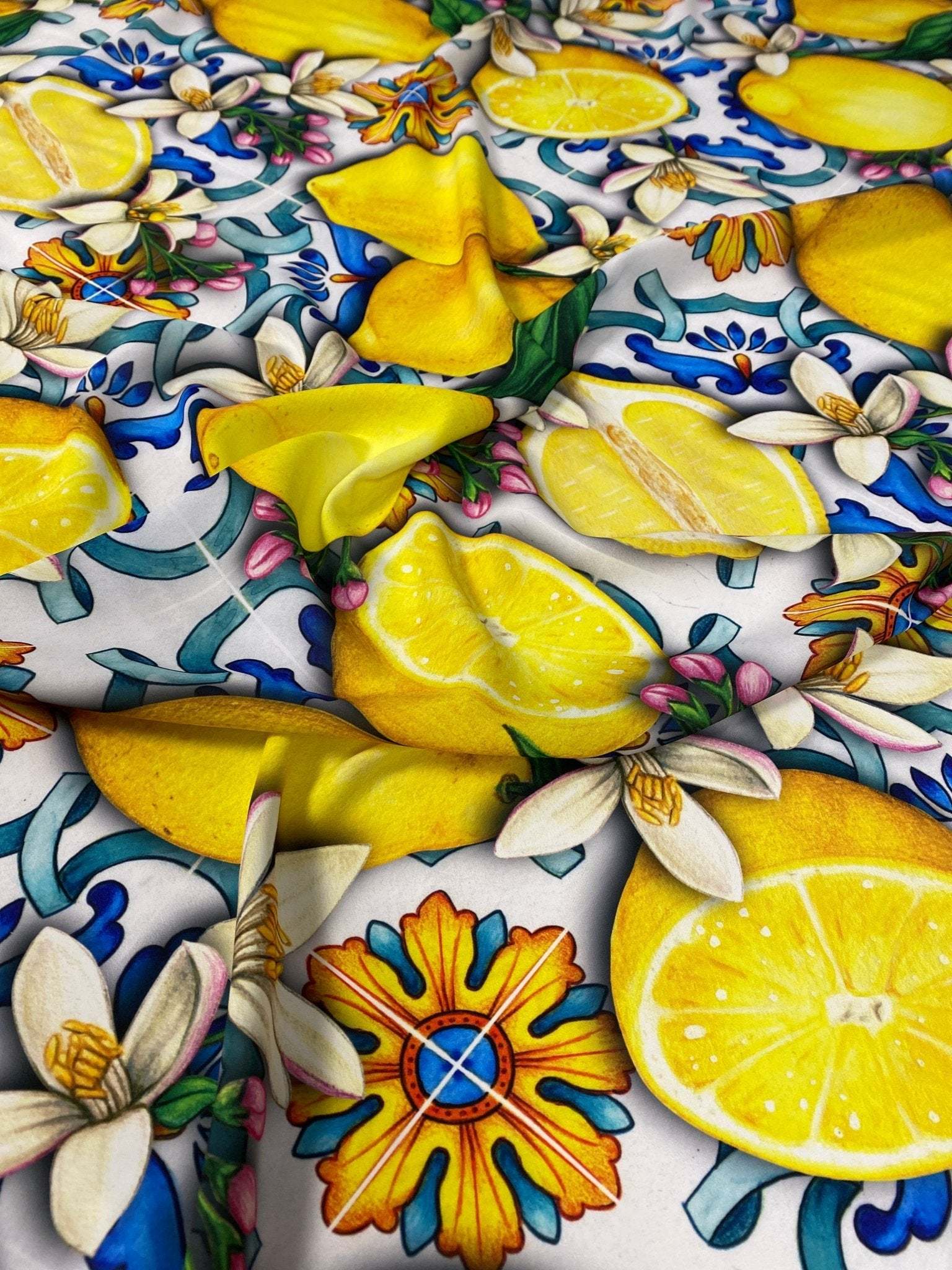 Close-up of lemon blue Spanish pattern fabric featuring vibrant yellow lemons, blue and orange floral motifs, and green leaves on a white background