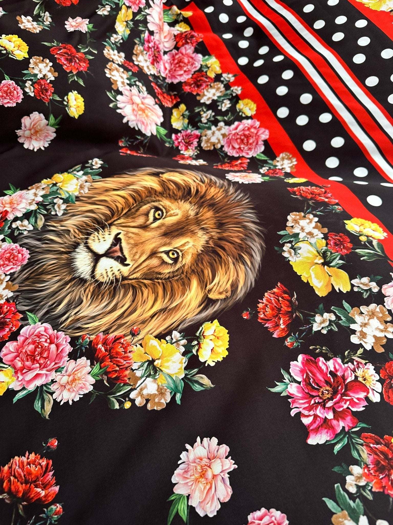 Floral print fabric with vibrant flowers and a lion illustration on black background with red and white striped polka dot border