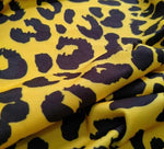 Close-up of yellow leopard pattern stretch fabric with black spots and soft texture