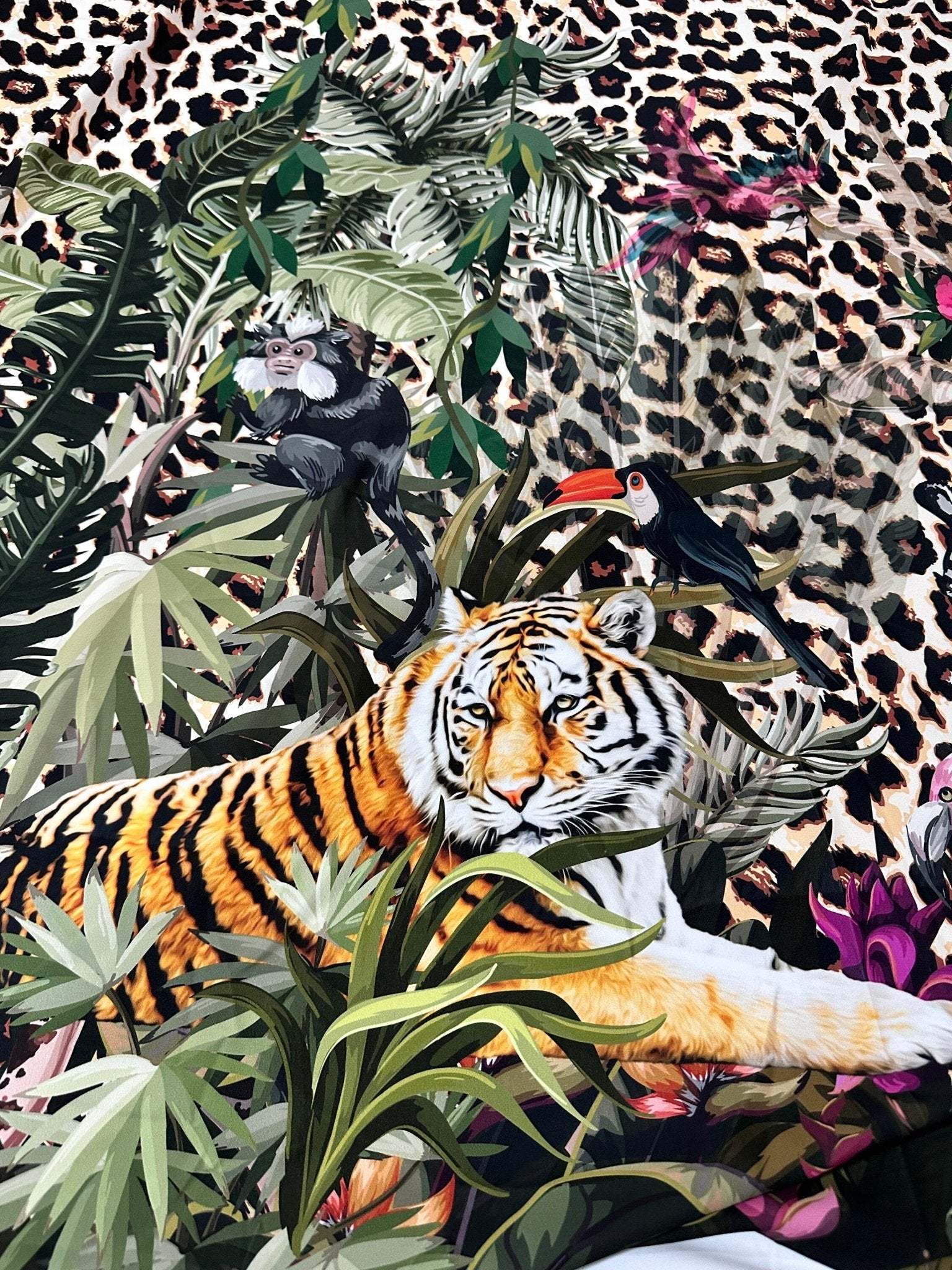 Leopard tropical leaf pattern fabric with jungle animals including a tiger, toucan, and monkey on leopard print background