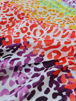 Colorful leopard print fabric with red, orange, yellow, purple, and black spots on a white background, ideal for sewing projects