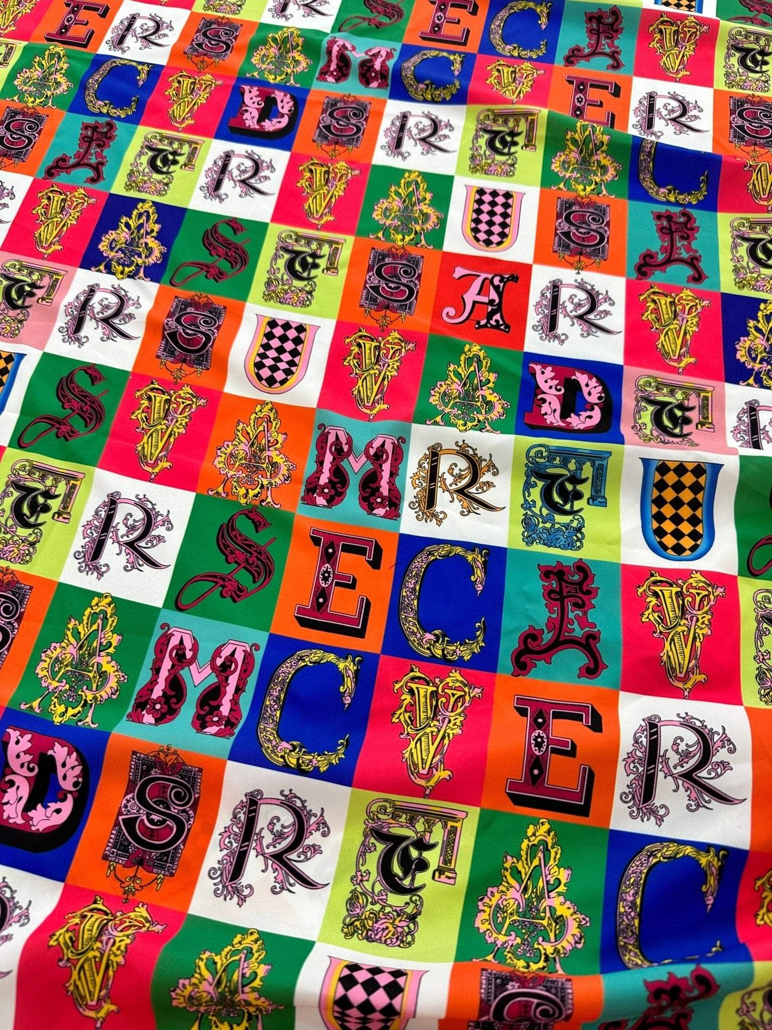 Colorful letter print cotton fabric with varied ornate alphabet designs on multi-colored squares, 150cm wide, ideal for sewing and crafting projects