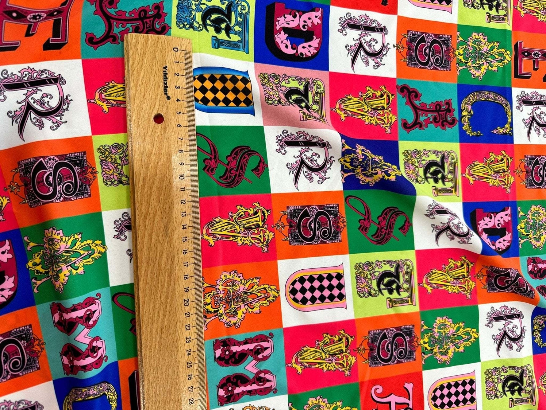 Colorful letter print cotton fabric with intricate designs and a wooden ruler for scale