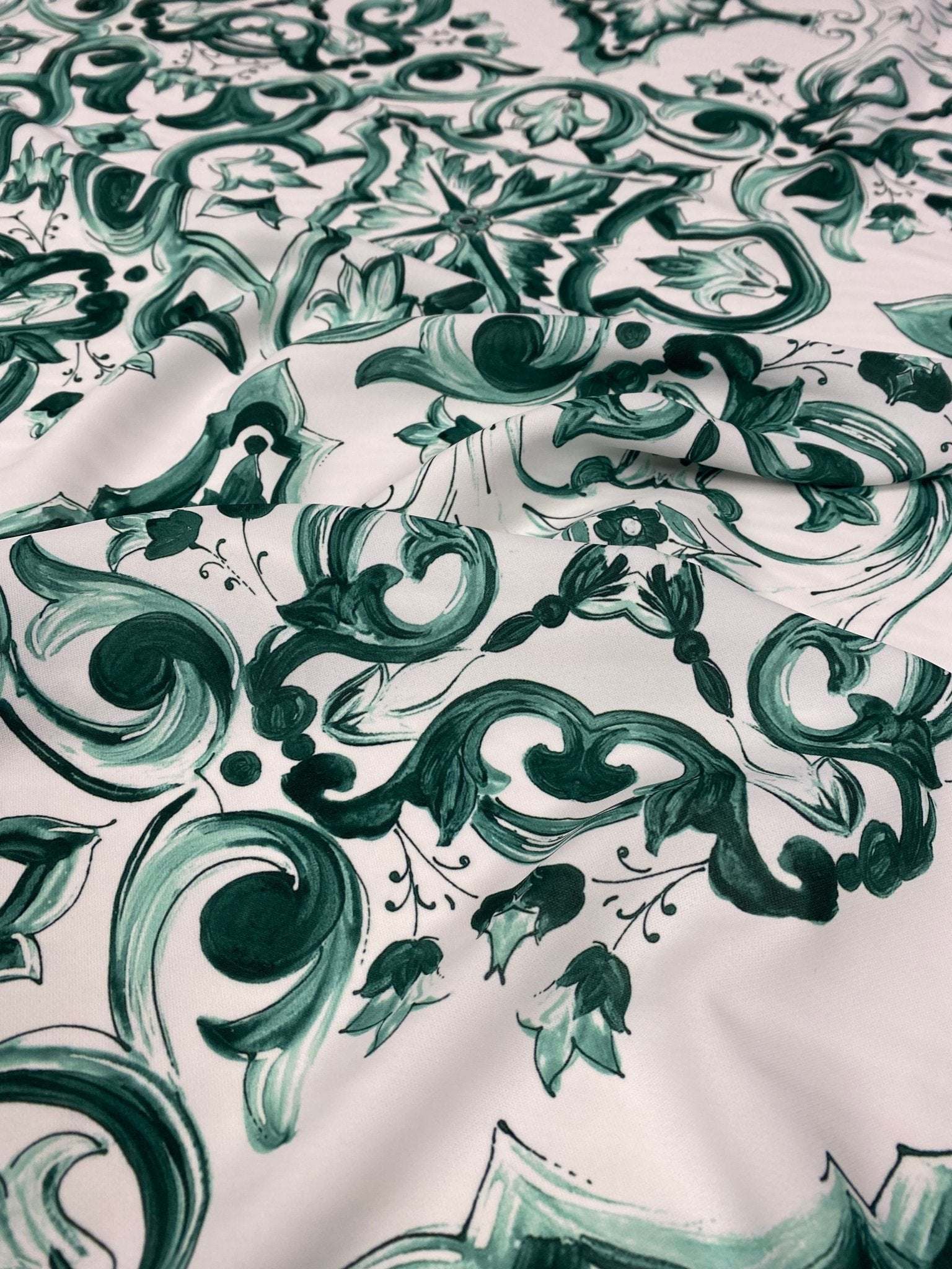 Close-up of green and white Majolica pattern fabric with intricate swirls and floral designs on 150cm wide textile