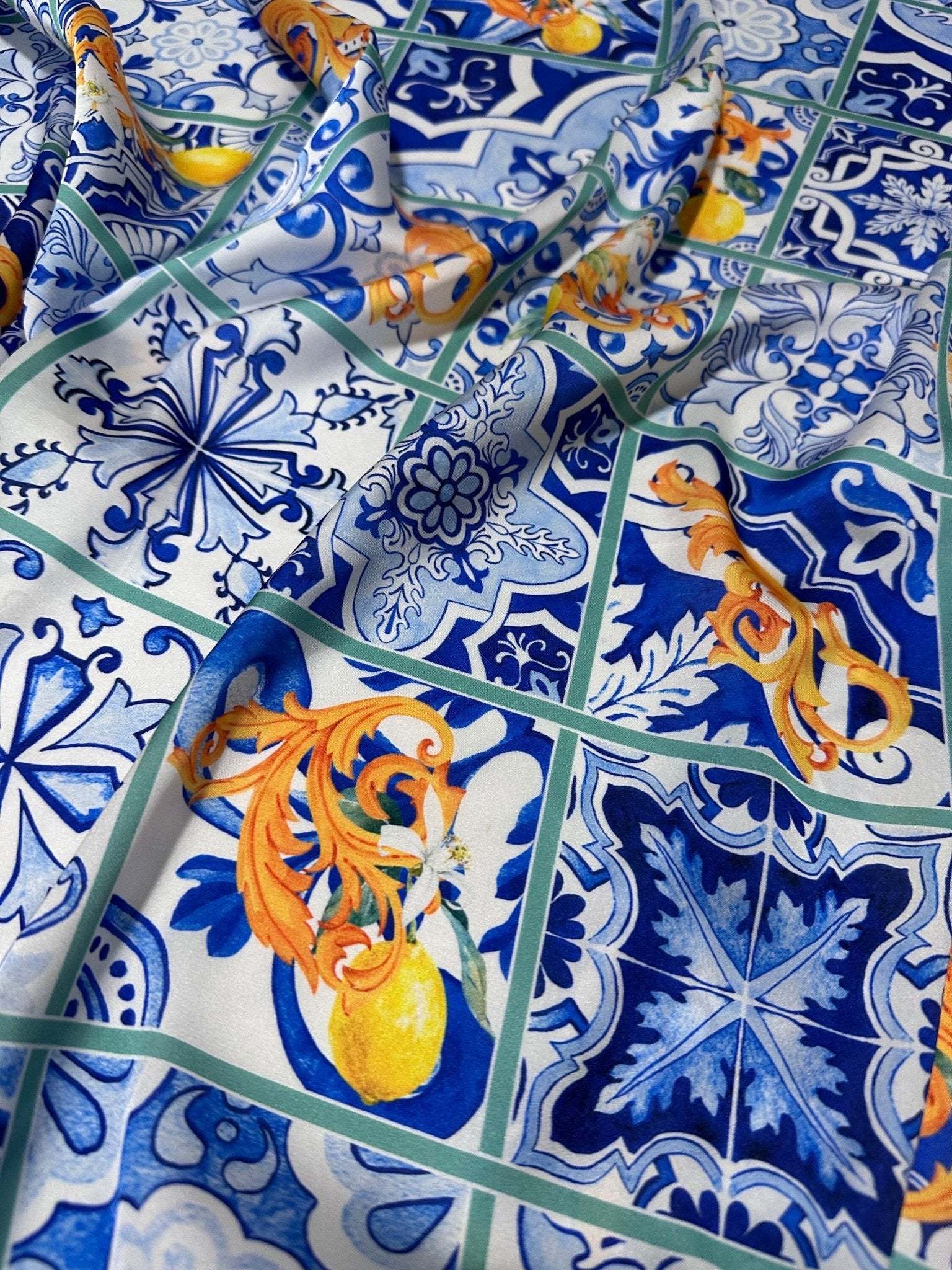 Close-up of Majolica Lemons Luxury Fabric featuring blue and white traditional tile patterns and vibrant yellow lemon motifs