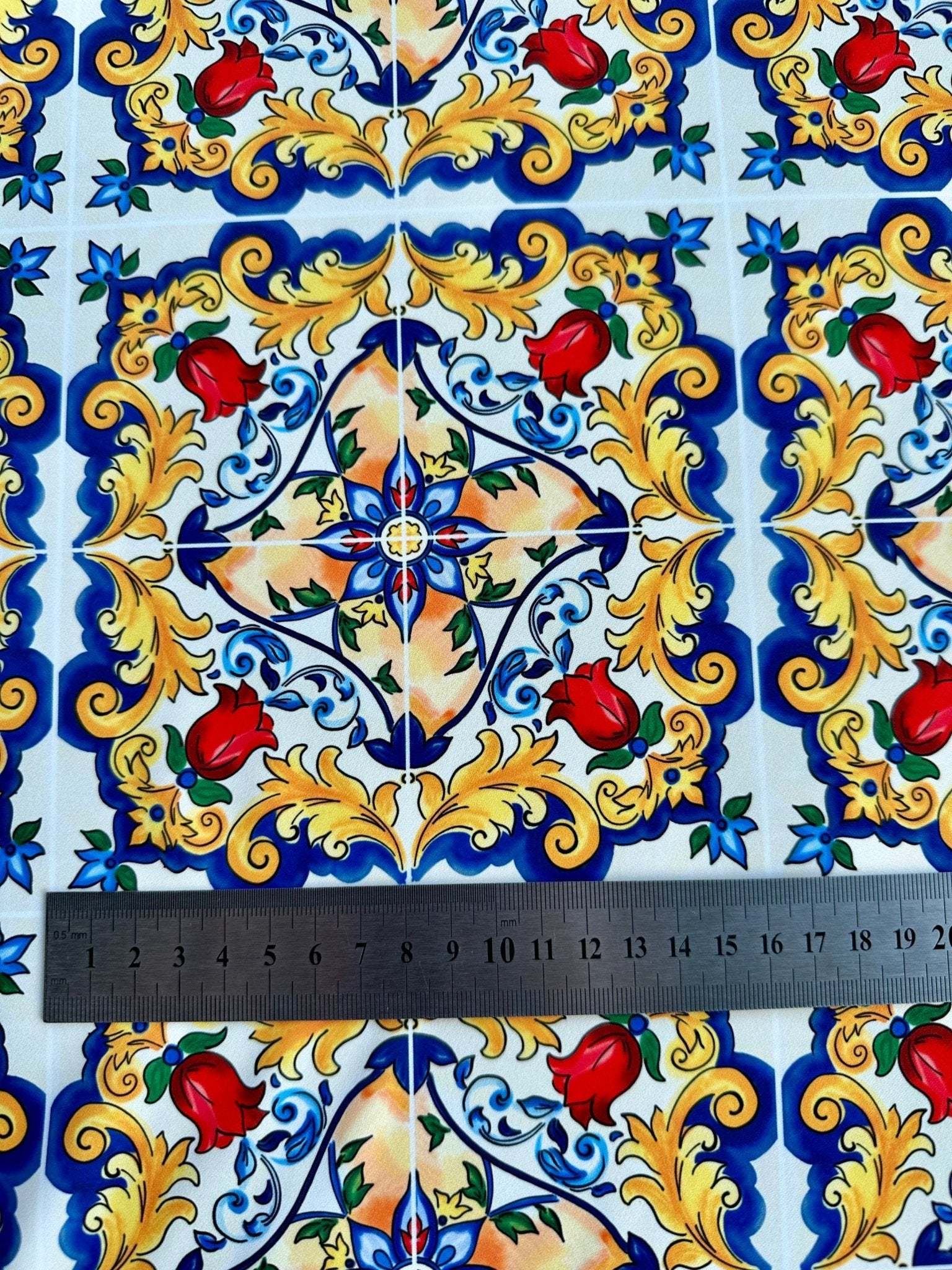 Close-up of Majolica Pattern Fabric with vibrant Sicilian-inspired floral and geometric design featuring red flowers and yellow ornate details next to a ruler for scale