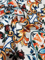 Close-up of Majolica Pattern Fabric with vibrant orange, blue, and green decorative motifs on a white background, showcasing soft and durable textile texture.