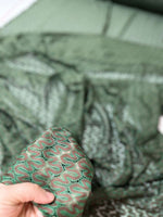 Close-up of green and brown zigzag knit jersey mesh fabric held in hand showing texture and pattern