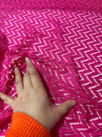 Hand touching bright pink zigzag knit jersey mesh fabric with a textured pattern for sewing and crafting projects