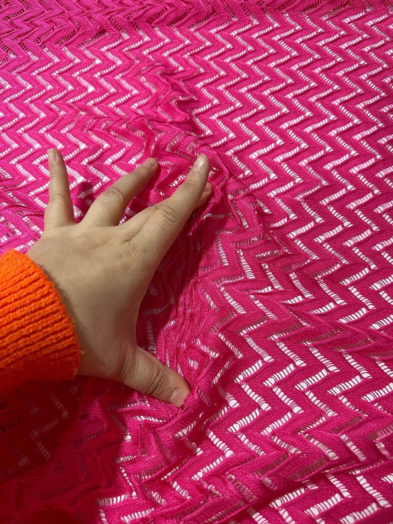 Hand touching vibrant pink zigzag knit jersey fabric with mesh texture for sewing and crafting projects