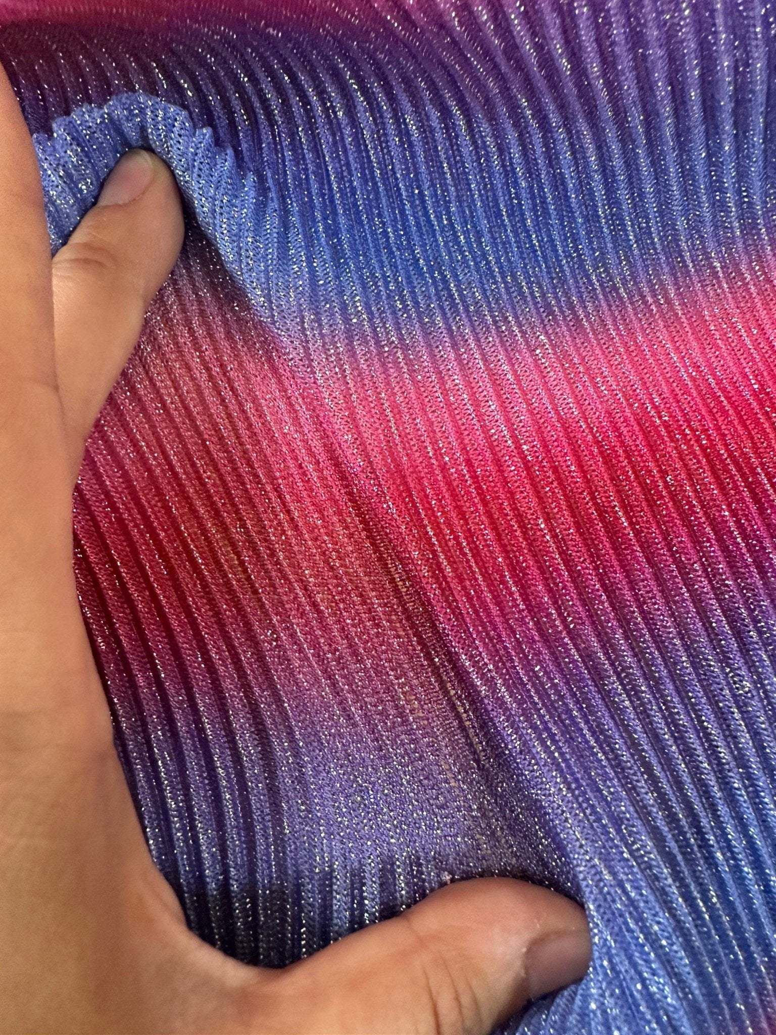 Close-up of pleated power mesh fabric in shimmering gradient shades of purple, blue, and pink held by hand