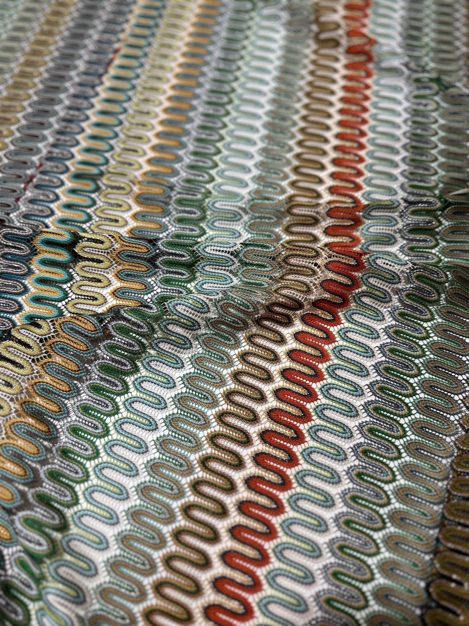 Close-up of colorful fabric with a zigzag mesh knit pattern in various colors including green, red, and brown