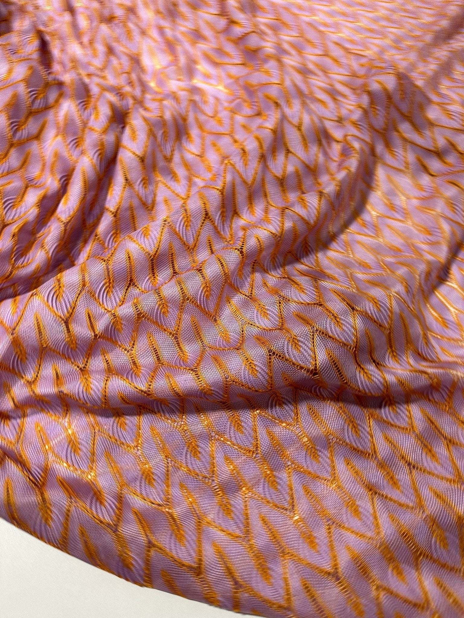 Close-up of lilac and orange zigzag knit jersey mesh fabric with lightweight texture for fashion and crafting projects
