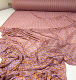 Roll of lilac and orange zigzag knit jersey mesh fabric spread out on white surface for crafting and fashion projects