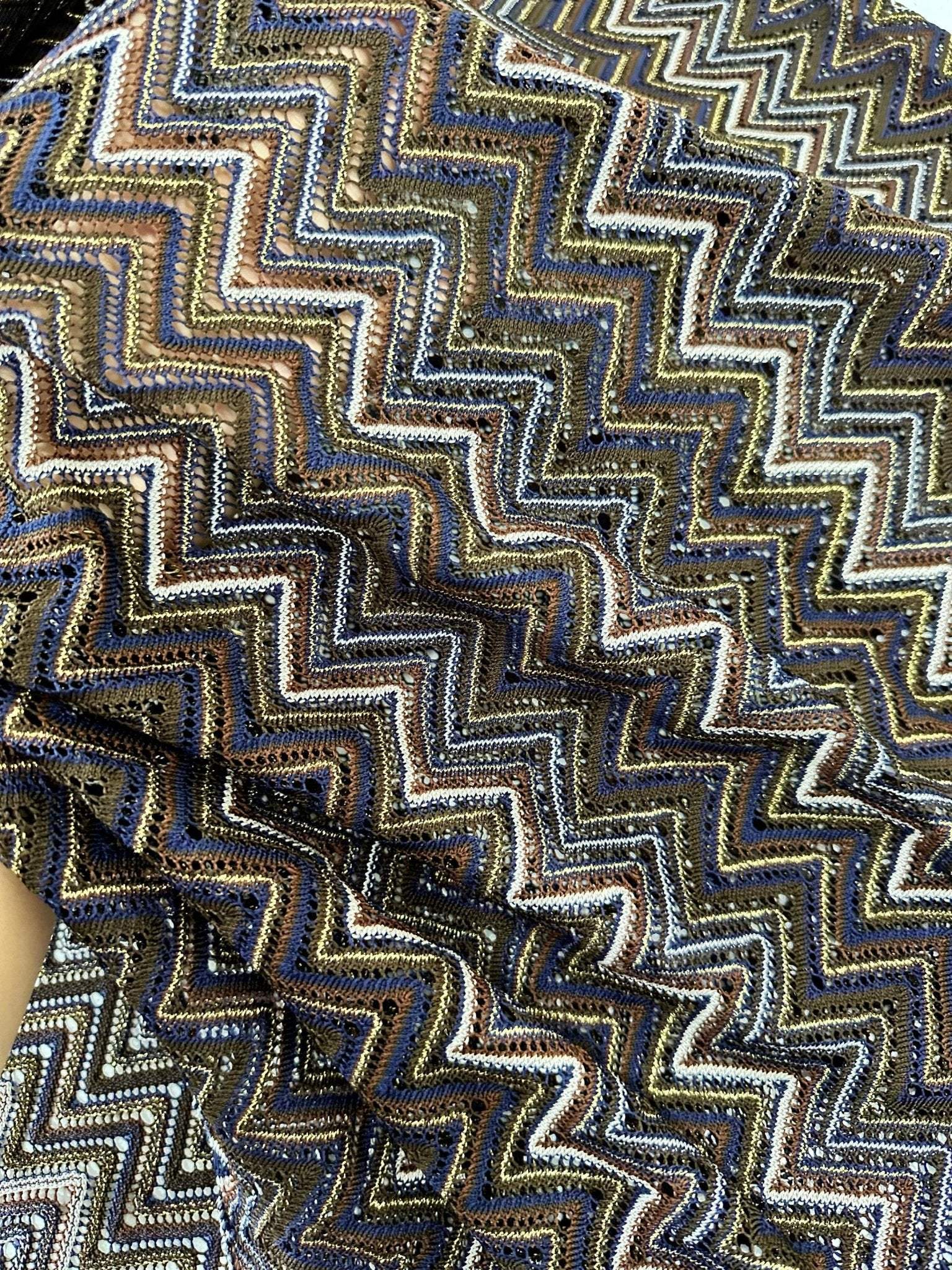 Shimmering zigzag knitted mesh fabric with elastic stretch and intricate pattern in gold, black, and silver tones