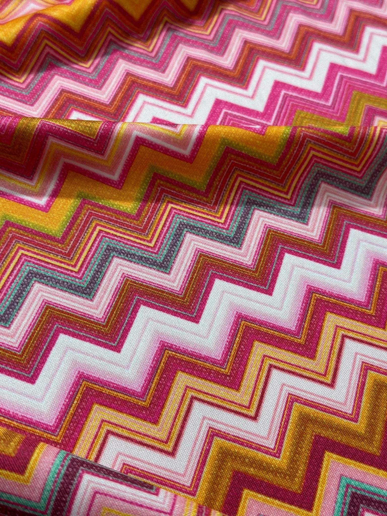 Close-up of colorful fabric with zigzag pattern featuring pink, gold, white, and gray tones and 4-way stretch for versatile use