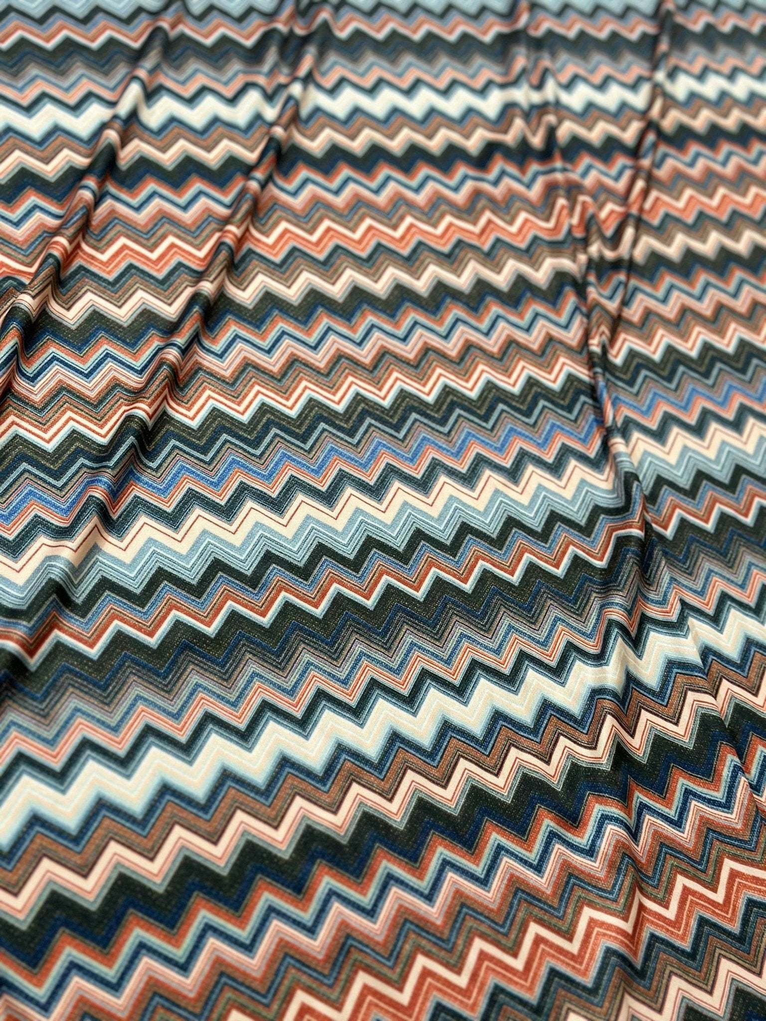 Close-up of multi-colored zigzag patterned 4-way stretch mesh fabric with blue, orange, and beige tones.