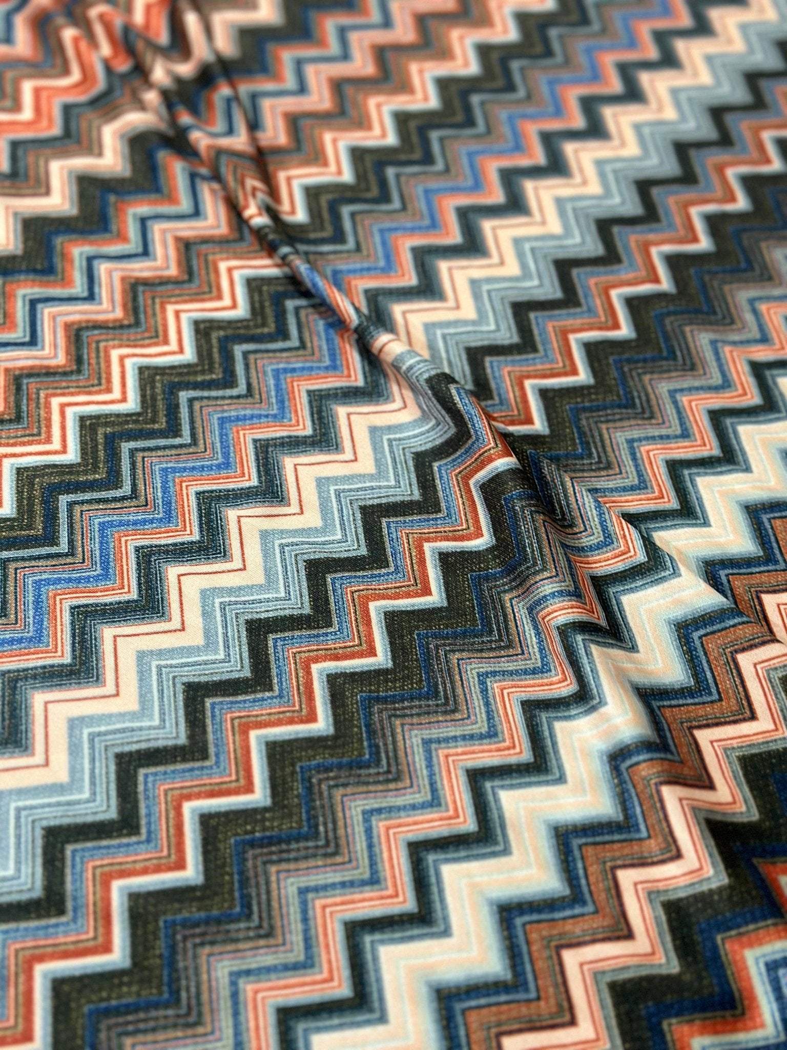 Close-up of flexible 4-way stretch mesh fabric with multicolored zigzag pattern in blue, orange, and beige tones