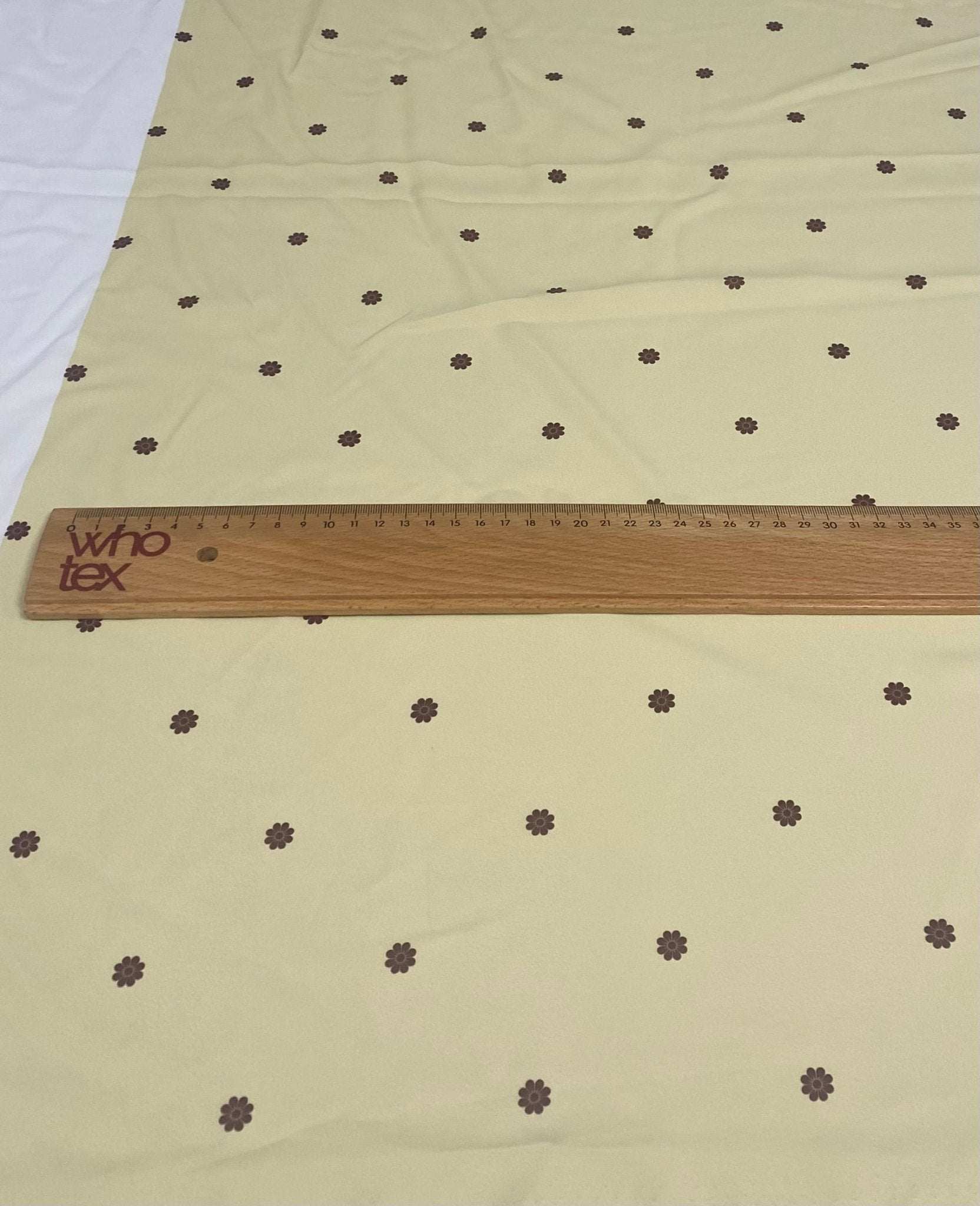 Minimal yellow fabric with small brown floral pattern and wooden ruler on top