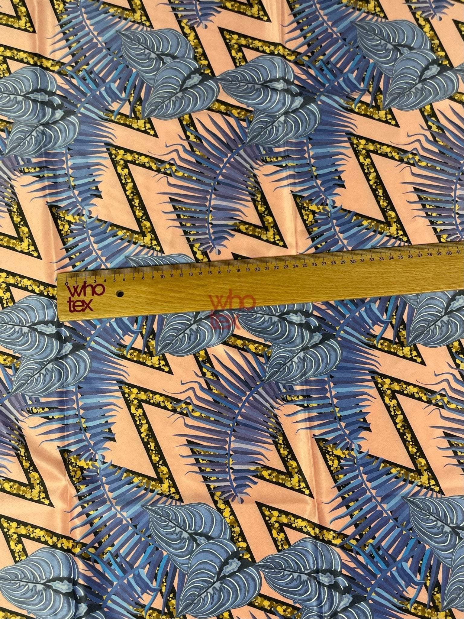 Modern geometric zigzag fabric pattern with blue tropical leaf print and measuring ruler on peach background