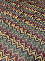 Multicolor chevron jacquard fabric with vibrant zigzag pattern in green, yellow, red, and black tones, ideal for sewing garments.
