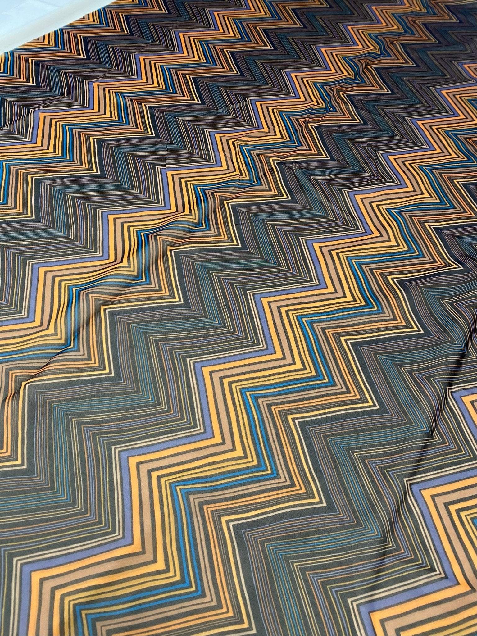 Multicolor chevron zigzag pattern fabric with vibrant blue, yellow, and dark tones, ideal for sewing and crafts.